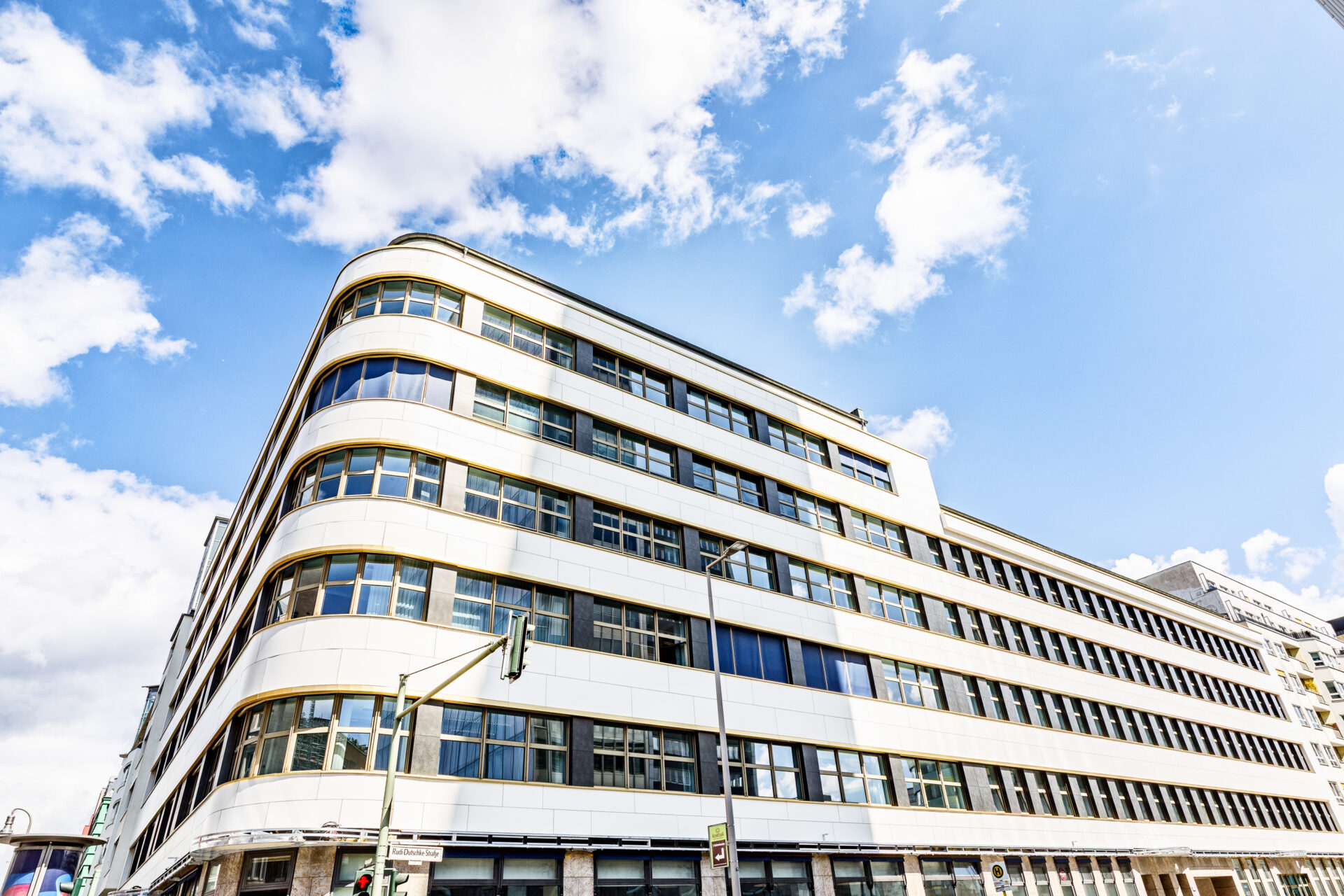 Bürokomplex Charlottenstraße / Rudi-Dutsche-Straße Moderne Architektur eines mehrstöckigen Gebäudes mit geschwungener Fassade und großen Fenstern vor einem blauen Himmel.
