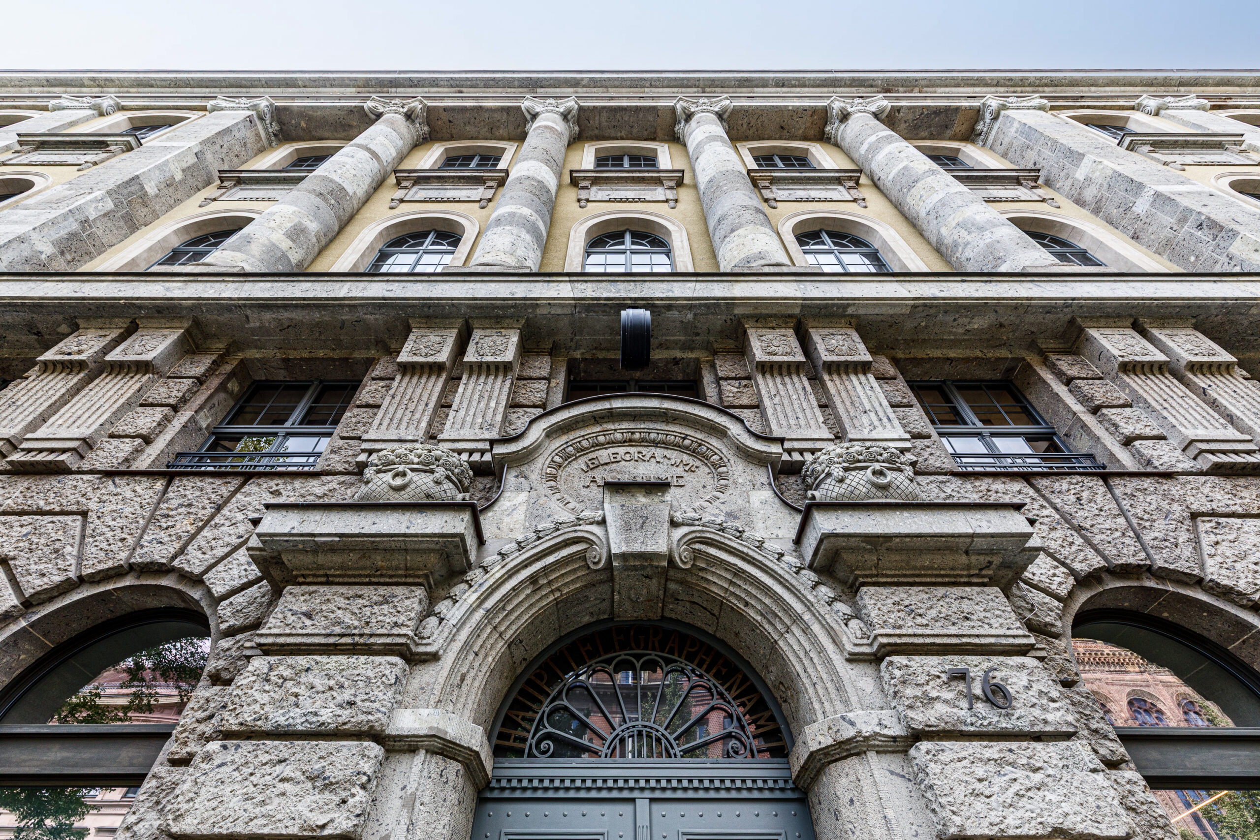 Historisches Gebäude mit detaillierter Steinfassade, Säulen und verzierten Fenstern. Eingangsbereich mit kunstvollem Gittertor und Reliefs.