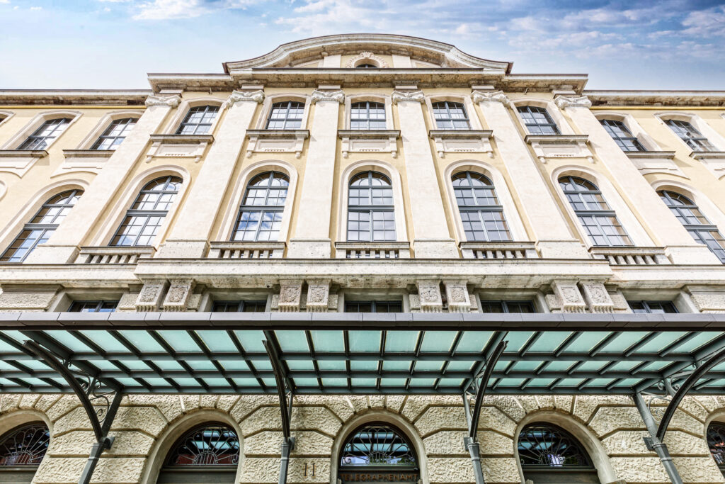 Historisches Gebäude mit mehreren großen Fenstern und einem Vordach aus Glas. Ehemaliges Telegrafenamt, verziert mit architektonischen Details.