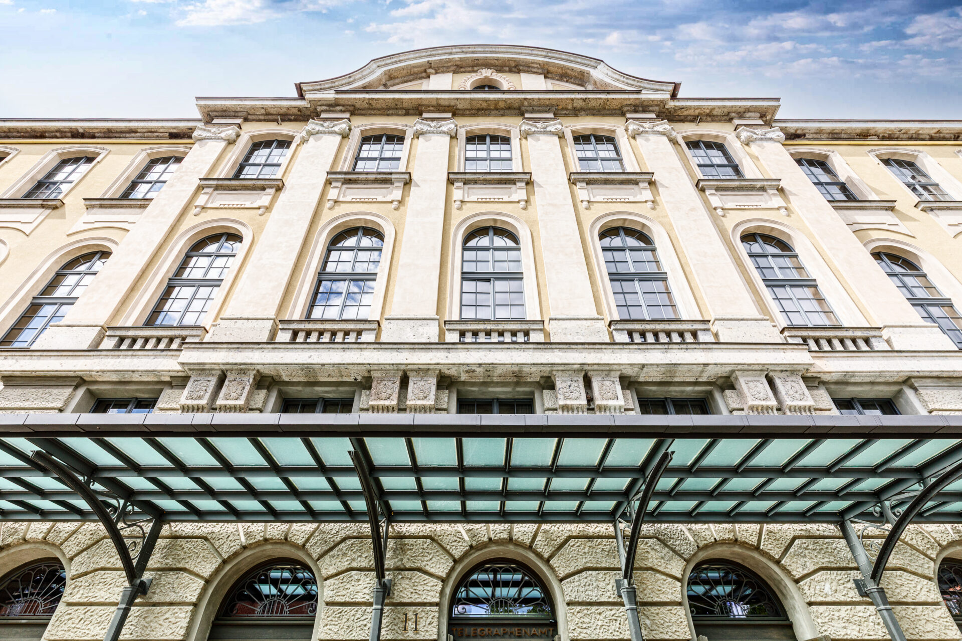 Historisches Gebäude mit mehreren großen Fenstern und einem Vordach aus Glas. Ehemaliges Telegrafenamt, verziert mit architektonischen Details.